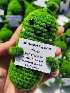 a hand holding a small green stuffed animal with a sign in it's mouth