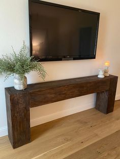 a tv mounted on the wall next to a wooden bench with vases and candles