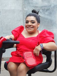 a woman in a red dress is sitting on a black chair and smiling at the camera