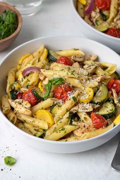 a white bowl filled with pasta covered in chicken and veggies next to a fork