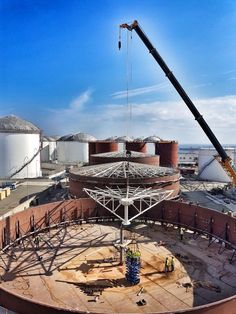 a crane that is standing on top of a building near some silo's