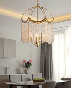 a chandelier hanging over a dining table in a room with white walls and curtains