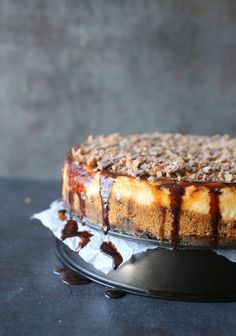 a cheesecake with chocolate sauce and nuts on top is sitting on a cake platter