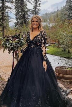 a woman wearing a black dress standing in front of trees