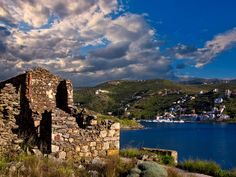 an old stone building sitting on top of a hill next to a body of water