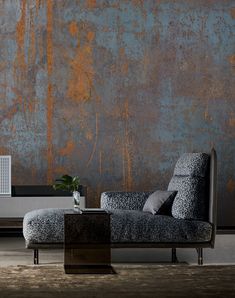 a couch sitting in front of a wall with rust on it's side and a table next to it