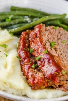 meatloaf with mashed potatoes and asparagus on a white plate, ready to be eaten