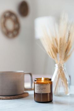 a candle sitting on top of a table next to a cup and vase filled with wheat