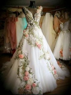 a wedding dress with flowers on it in a room full of other gowns and dresses