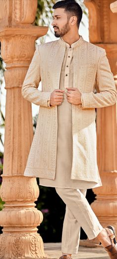 a man wearing a white sherwa with a beige jacket and pants on his feet