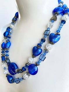 "Beautiful hand beaded dual strand blue necklace. This lovely necklace consists of many different types of blue hued beads with some clear crackle beads mixed in.  Some of the larger beads are in a heart shape.   This has been created to provide a look that is both interesting, unique and elegant.   The clasp is very showy and easy to clasp, I like easy! Measurements: When clasped, the length of the shortest strand is 23\"	in stock	42.00 USD	"	0.00 USD	Weddings > Jewelry > Necklaces
https://i.et Blue Glass Beaded Necklaces For Party, Blue Glass Heart Beads Jewelry, Blue Glass Jewelry With Heart Beads, Elegant Blue Beaded Necklace With Heart Beads, Blue Double Strand Necklaces For Party, Blue Double Strand Necklace For Party, Blue Glass Beads For Jewelry Making, Blue Glass Beads For Gifts, Blue Glass Beads For Gift