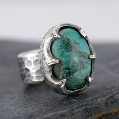 .999 Fine silver ring with a Chrysocolla gemstone. US Ring Size 8 Chrysoprase gemstone measures 2.1cm by 1.5cm Ring band width: 1.1cm Handmade by Mike Summers. We are husband and wife Mike and Annie, making silver jewelry in two uniquely different styles. With a passion for rocks and gemstones, we also cut and polish our own cabochons to use in our creations. We live and work in a tiny cabin in a remote part of Talkeetna in Alaska and it's always a bit of an adventure crossing our creek in a boat to get on the roads to the post office. We have set our dispatch time to 1-2 weeks, and we usually make a visit to the post office once a week all being well. We do not want anyone buying from us to be disappointed if you need a quick delivery, so please feel free to contact us before ordering and Oval Chrysocolla Jewelry With Patina, Artisan Chrysocolla Gemstone Rings, Unique Cabochon Emerald Ring, Sterling Silver Emerald Ring With Large Stone, Silver Emerald Cabochon Ring, Gift Ring With Large Chrysoprase Stone, Unique Oval Emerald Ring In Sterling Silver, Oval Emerald Ring With Large Stone In Sterling Silver, Unique Chrysocolla Rings As Gift