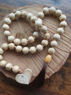 a wooden bead necklace with a tassel and heart charm on it sitting on a piece of wood