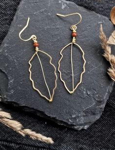 a pair of gold earrings sitting on top of a rock next to some dried leaves