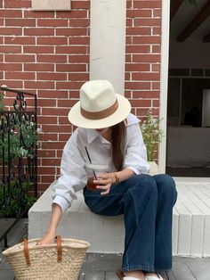 This is a stylish Panama-style hat, featuring a wide brim and a classic white colour, made from lightweight woven straw material. The hat is adorned with a beige fabric band around the crown, giving it a timeless and elegant appearance. The natural fibres make it breathable, making it an ideal accessory for warm weather. It pairs well with casual outfits, as seen here with the loose white blouse and relaxed jeans, and offers both sun protection and a chic, laid-back vibe. Its versatile design ma Casual White Boater Hat With Flat Brim, White Flat Brim Boater Hat For Vacation, Cream Wide Brim Felt Hat For Summer, Summer Wide Brim Cream Fedora, Cream Panama Hat With Curved Brim For Summer, Chic Cream Felt Hat For Summer, Summer Cream Wide Brim Fedora, Classic White Curved Brim Sun Hat, Casual White Straw Boater Hat