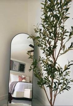 a mirror sitting on top of a table next to a potted plant in front of a bed