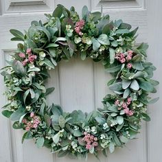 a green wreath with pink flowers and greenery hangs on the front door of a house