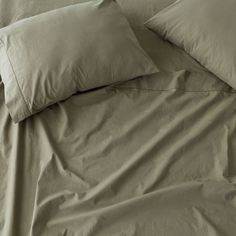 a bed with three pillows and two pillow cases on top of it, all covered in beige linens