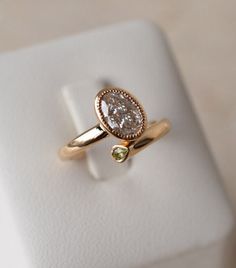 a gold ring with a pear shaped diamond on it sitting on a white surface in front of a box