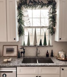 a kitchen decorated for christmas with evergreen garland on the window sill and pine cones