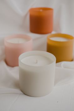 three different colored candles sitting on top of a white cloth covered tablecloth, with one lit candle in the middle