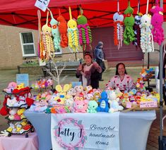 two women standing behind a table with stuffed animals on it and decorations hanging from the ceiling