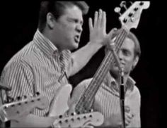 two men are playing guitars and singing into microphones while one man is holding his hands up