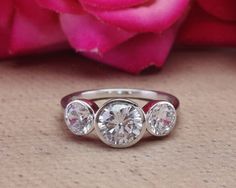 three stone ring with rose in the background