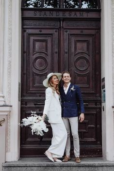 a man and woman standing in front of a wooden door with flowers on the steps