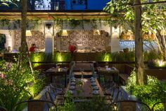 an outdoor dining area with tables and chairs surrounded by greenery at night in the city