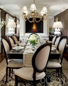 a dining room table with chairs and a chandelier hanging from the ceiling in front of a fireplace