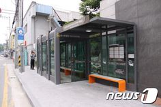 an empty bus stop on the side of a street with people walking by it and there is a man standing in the doorway