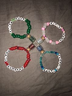 four bracelets with beads and charms on a bed sheet, one has a bottle