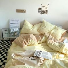 an unmade bed with yellow sheets and pillows on top of it next to a black and white checkered floor