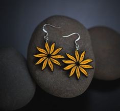 two yellow flower shaped earrings sitting on top of a rock next to some rocks and pebbles