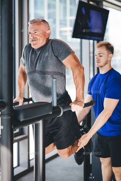 an older man doing pull ups in the gym with his trainer - stock photo - images