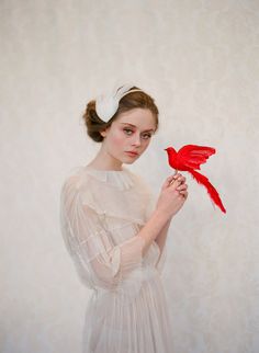 a woman holding a red bird on top of her finger while wearing a white dress