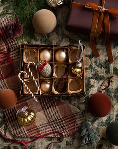 an assortment of christmas ornaments in a box on a plaid tablecloth next to other holiday decorations