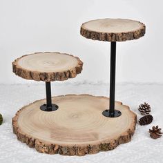 two wooden slices with black metal legs and pine cones on the bottom one is round