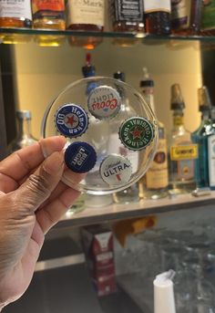 a hand holding a glass ball with several different types of buttons on it in front of liquor bottles