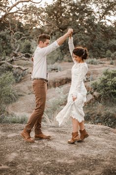 a man and woman dancing on top of a rock in the desert with trees behind them