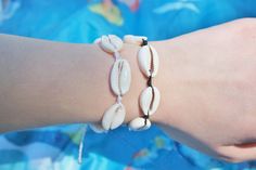 two bracelets with seashells on them are being held by a woman's hand