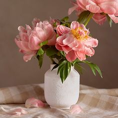 pink flowers are in a white vase on a plaid tablecloth with petals scattered around