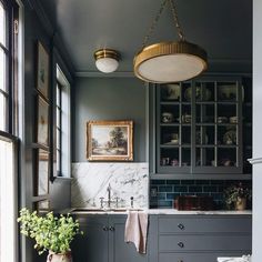 a kitchen with gray cabinets and marble counter tops, gold accents on the light fixture