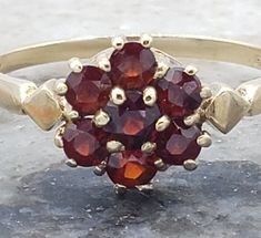 This vintage ring has me believing in the flowers of spring. The juicy red garnets sparkle and shine in this lovely ring.  The history of garnet dates back to the Bronze Age, more than 5000 years ago. Its name, which has been used since these ancient times, was derived from the Latin word granatium, which means pomegranate (because the small, red crystals were thought to resemble pomegranate seeds). Garnet has been believed to be extremely beneficial in the realm of business as well. The stone c Vintage Garnet Birthstone Ring In Yellow Gold, Vintage Yellow Gold Garnet Birthstone Ring, Vintage Garnet Birthstone Promise Ring, Vintage Garnet Birthstone Rings, Vintage Gold Garnet Birthstone Ring, Vintage Garnet Promise Ring, Vintage Oval Garnet Birthstone Ring, Vintage Red Garnet Cluster Ring, Vintage Garnet Cluster Ring As Gift