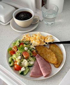 a white plate topped with meat and vegetables next to a cup of coffee