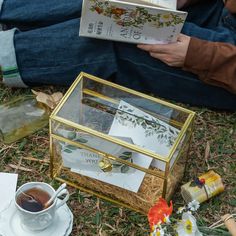 a person sitting on the ground reading a book next to a glass box with cards inside