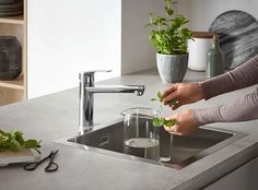 a woman is washing leaves in a sink with a faucet next to it