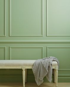 a white bench with a blanket on it in front of a green wall and wooden floor