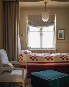 a bed sitting under a window in a bedroom next to a chair and footstool